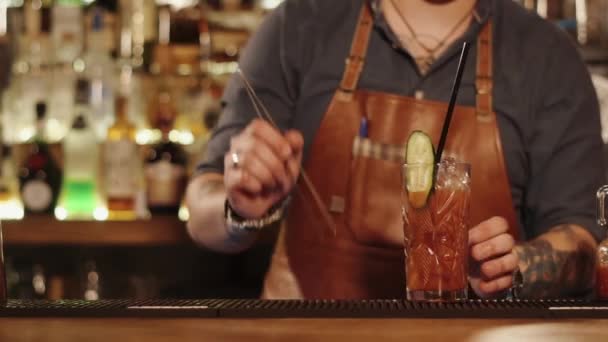 close shot at the barman hands, the man puts the cucumber and straw in a glass with juice - Footage, Video