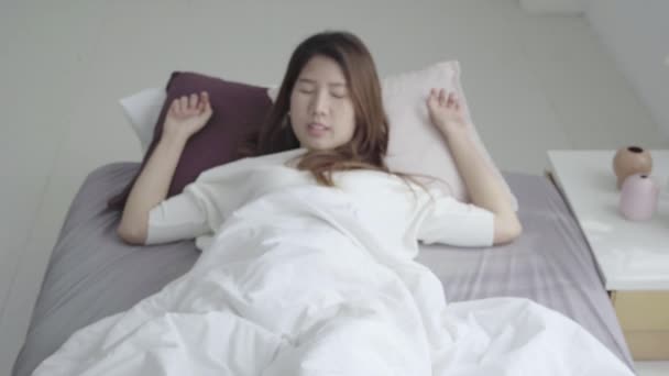 Happy beautiful young Asian woman waking up in morning, sitting on bed, stretching in cozy bedroom, looking through window. Funny asian woman after wake up. Asia woman is stretching and smiling. - Video