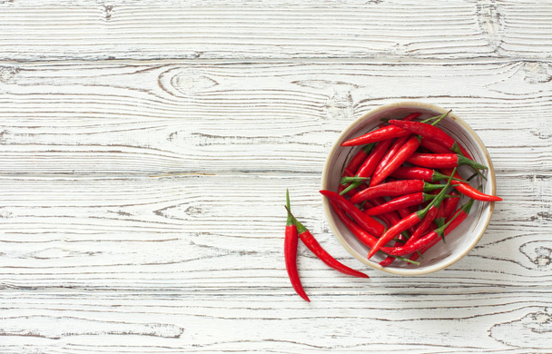 Chilli peppers in clay pot over white wood background - Foto, Bild