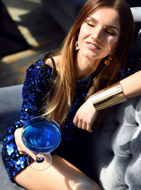 fashion brunette woman sitting in expensive interior restaurant drinking drinking blue margarita cocktail looking at the corner - Foto, Imagem