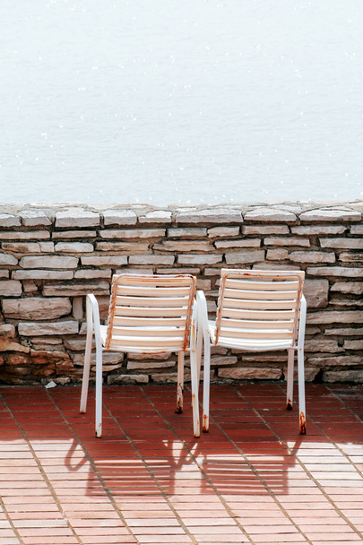 Sillas blancas en un balcón. Tradicional playa mediterránea y tiempo de descanso en la terraza sillas viejas blancas y el increíble mar azul. Sillas vacías miran hacia el mar, rodeadas por un muro de piedra
. - Foto, imagen