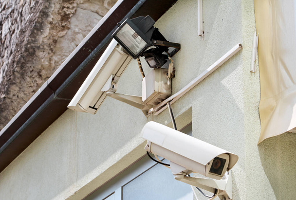 Bezpečnostní kamery a reflektor na zdi domu a budovy, zblízka. Zabezpečení domů fotoaparát ochranu, soukromí, bezpečí proti zločinu & dohled, namontované na vnější zdi domu. - Fotografie, Obrázek