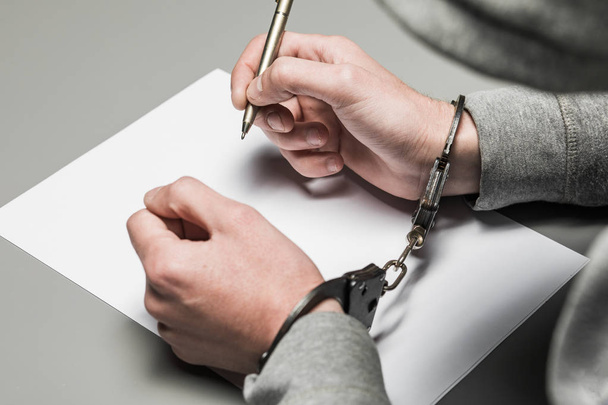 Les mains du criminel menotté écrivent une poignée sur du papier. Aveux sincères, demande, déclaration. Justice
. - Photo, image