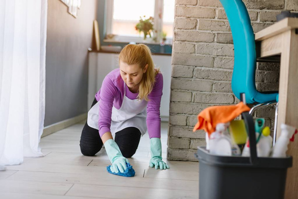 Žena v bílé zástěře čištění podlahy na kolenou - Fotografie, Obrázek