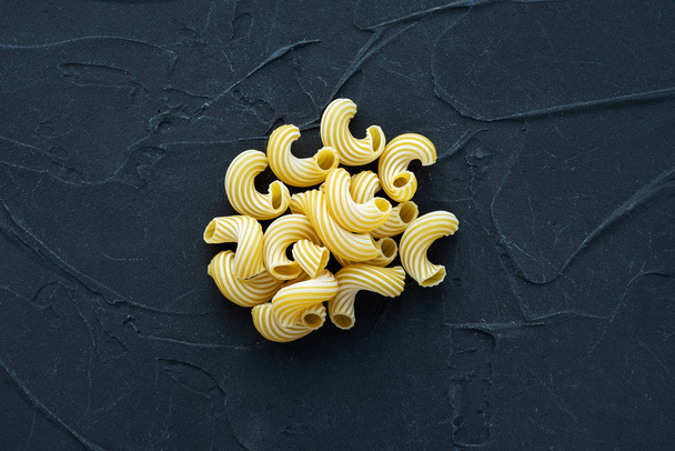 Macaroni rigati background with pasta on a black background. A view from the top, a close-up of a texture. - Photo, Image