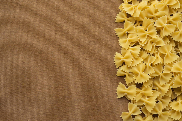 farfalle macaroni Beautiful decomposed pasta with the right, on its side on a rustic brown textured background. Close-up view from the top. Free space for text. - Fotoğraf, Görsel