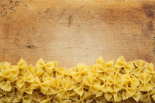 farfalle macaroni Beautiful decomposed pasta with a bottom on a wooden plank texture background. Close-up view from the top. Free space for text. - Fotoğraf, Görsel