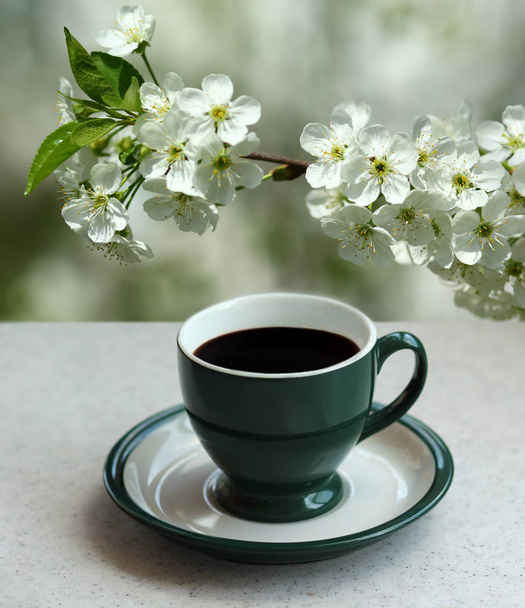 Taza verde de café expreso negro y una rama de albaricoque floreciente en el jardín
 - Foto, Imagen