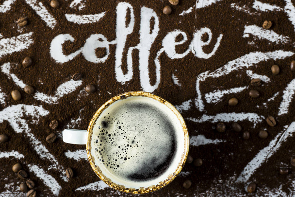 Een kopje verse warme koffie met schuim naast het woord "koffie" geschreven op de gemalen koffie - Foto, afbeelding