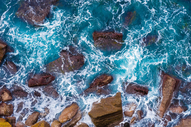 Top aerial view of blue waves crashing on rocky Australian coastline. Summer seascape with ocean waves and cliffs. Travel concept background - Photo, Image