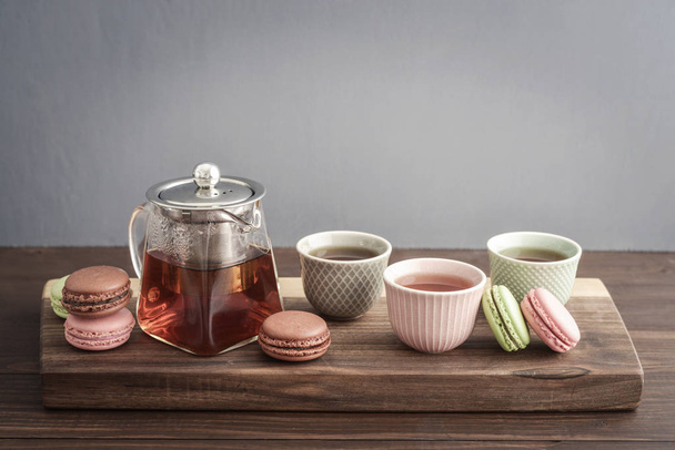 Different kinds of macaroons with glass teapot and cups on grey  background closeup - Фото, изображение