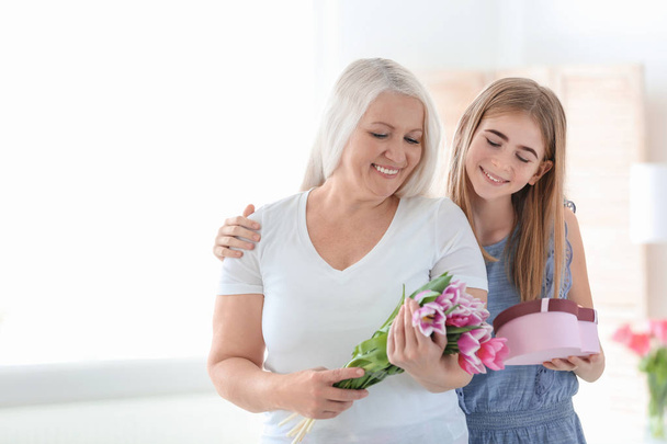 Happy mature woman receiving bouquet and gift from her teenage granddaughter at home - Foto, immagini