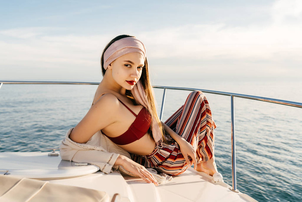 a luxurious stylish girl in summer clothes rests on her white yacht, enjoys the view of the sea and the sun - Foto, Bild