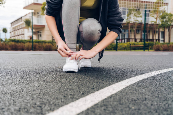 молода дівчина тренується на відкритому спорті, зв'язує взуття на кросівки
 - Фото, зображення