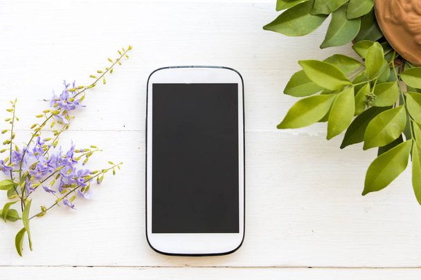 mobiele telefoon met oortelefoon en bloem op witte achtergrond - Foto, afbeelding