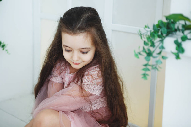 Une jeune fille aux cheveux longs dans une robe rose encadrée de feuilles vertes. Bouclez-vous. En regardant la caméra
. - Photo, image