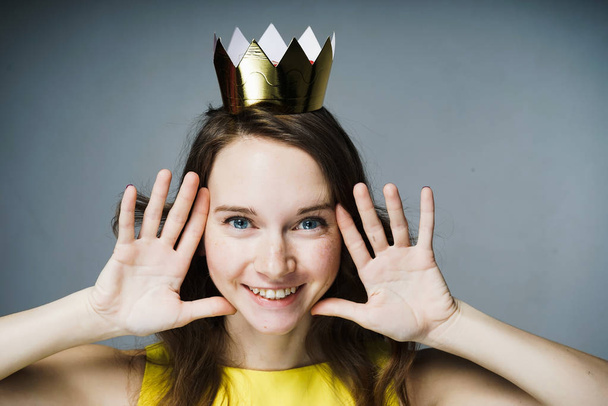 happy blue-eyed girl in a yellow dress smiles, on her head a golden crown - Photo, Image