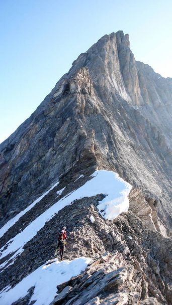 guida alpina che conduce due clienti maschi su un crinale roccioso e poi su un'alta vetta alpina - Foto, immagini