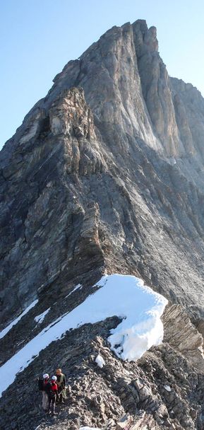 guide de montagne conduisant deux clients masculins à une crête rocheuse et vers un sommet alpin élevé - Photo, image