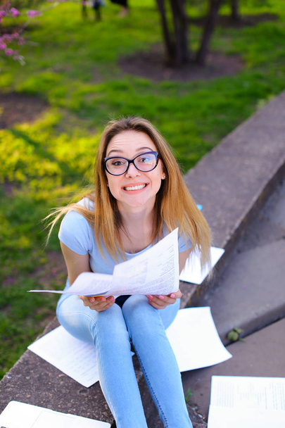 Estudiante bastante femenina leyendo papeles y jugando con el pelo en el parque de primavera
. - Foto, imagen