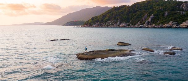 Male person fishing on a sea from the rock at sunset - Photo, Image