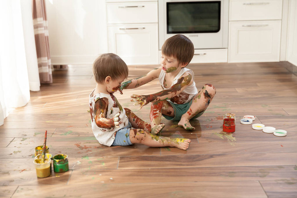 Δύο αγόρια, δύο αδέλφια παιχνιδιάρικα χρώματα κάθε άλλο κάθεται στο πάτωμα. - Φωτογραφία, εικόνα