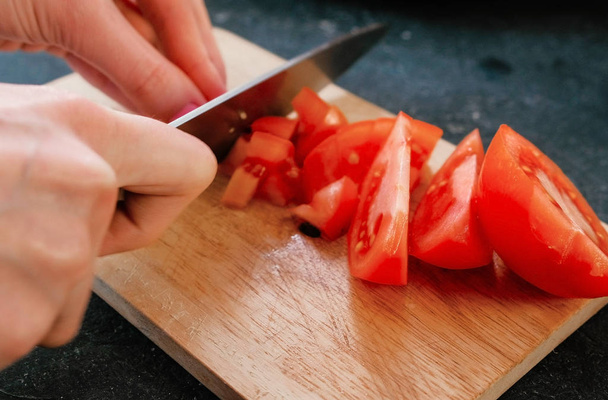 Closeup womans hands cutting tomatoes on a wood board. - Фото, изображение