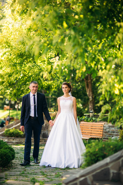 Νεαρό ζευγάρι, νύφη και γαμπρός περπατώντας και απολαμβάνοντας την ημέρα του γάμου τους. Ηλιοφάνεια. Το καλοκαίρι - Φωτογραφία, εικόνα