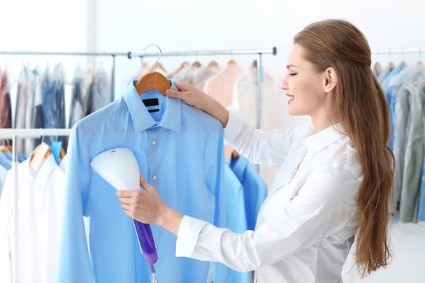 Young woman steaming shirt at dry-cleaner's - 写真・画像