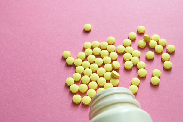 random yellow pills in white bottle on pink isolated background - Photo, Image