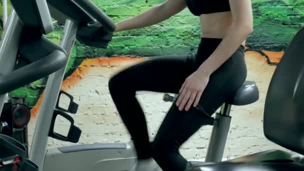 Fiatal, vonzó nő fokozása her tartóssági, miközben dolgozik egy exercycle. egy gyönyörű lány, az edzőteremben, helyhez kötött kerékpár portré. fiatal nő a gyakorlás kerékpár aerob testmozgás - Felvétel, videó