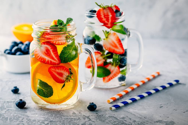 Infused detox water with orange, strawberry, blueberry and mint. Ice cold summer cocktail or lemonade. - Photo, Image