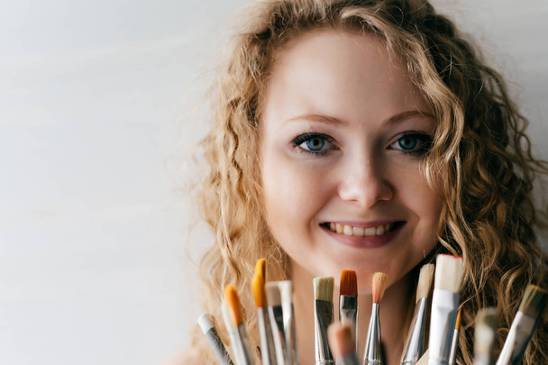 beautiful curly woman holding many different brushes, smiling and looking at the camera - Zdjęcie, obraz