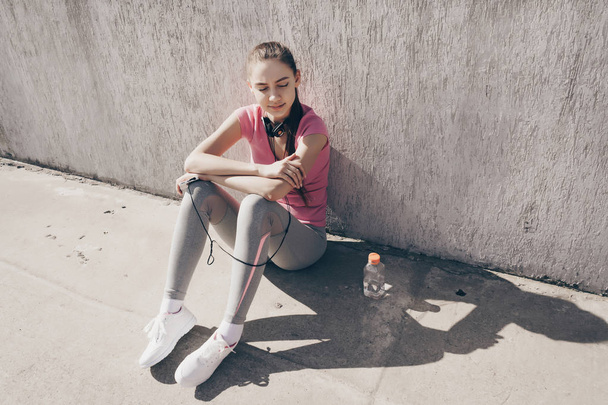 slender young girl sitting on the ground outdoors, resting after a difficult workout and fitness - Φωτογραφία, εικόνα