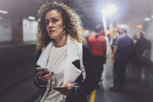 スマート フォンを用いた輸送プラットフォーム上のバックパックで魅力的な女性が地下鉄駅の鉄道の列車を待っている間列車の切符の写真を作る. - 写真・画像