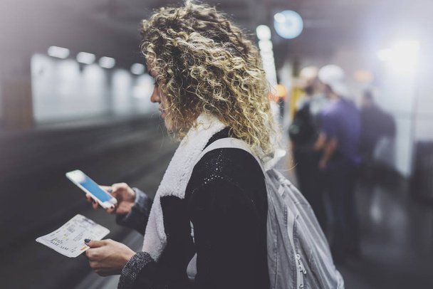 Attractive woman with backpack on transit platform using smartphone for make photo of train ticket while waiting rail train on metro station. - Foto, Imagen