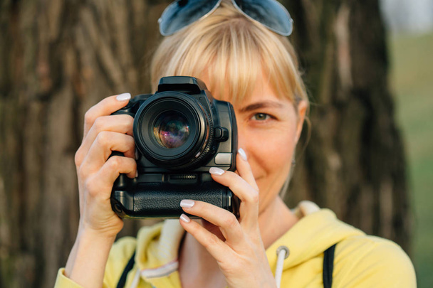 Girl with professional camera in hands. Close up of female photographer in park. - Foto, Imagen