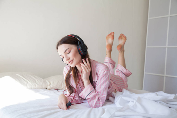 morena en pijama rosa escuchando música con auriculares en la cama
 - Foto, Imagen