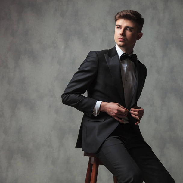 hombre de negocios sentado abotonando su traje y mirando al costado
 - Foto, Imagen