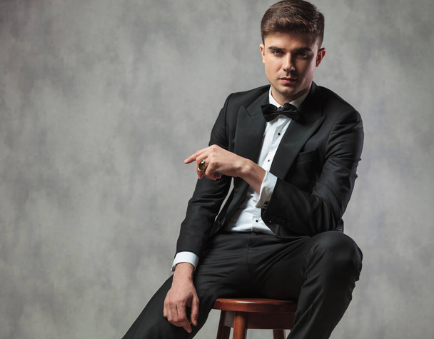 sexy gentleman dressed elegantly sitting and pointing to side - Zdjęcie, obraz