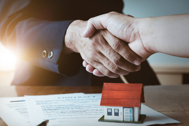 Agent nieruchomości, drżenie rąk, z jego klient po podpisania umowy, dokument umowy i dom modelu na biurko z drewna - Zdjęcie, obraz