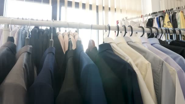 Kleiderbügel voller unterschiedlicher Kleidung in einem Geschäft neben einem Fenster - Filmmaterial, Video