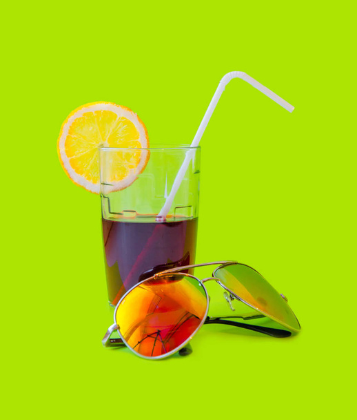 Fresh Juice glass with a straw slice of yellow lemon and sunglasses on a green background. Fashion pastel summer design style concept - Foto, Imagen