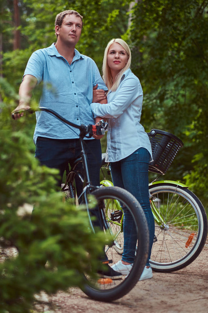 Un couple attrayant d'une femme blonde et d'un homme vêtus de vêtements décontractés, embrasser près d'un vélo dans un parc
. - Photo, image