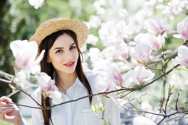 春の庭でマグノリア ピンクの花の木の周りの麦わら帽子の若い美しさ女性 - 写真・画像