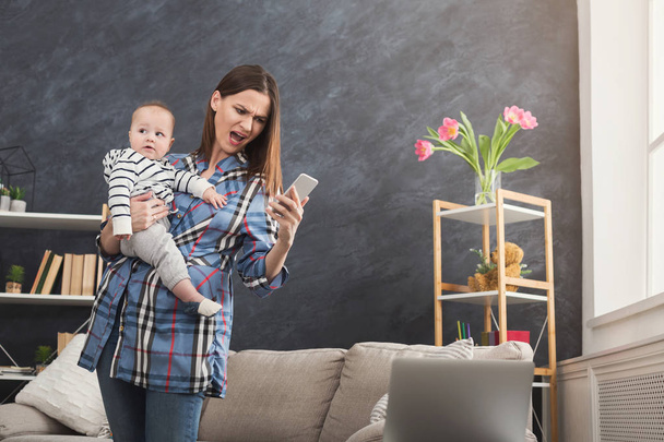 Angry mother holding baby while using phone - Photo, Image