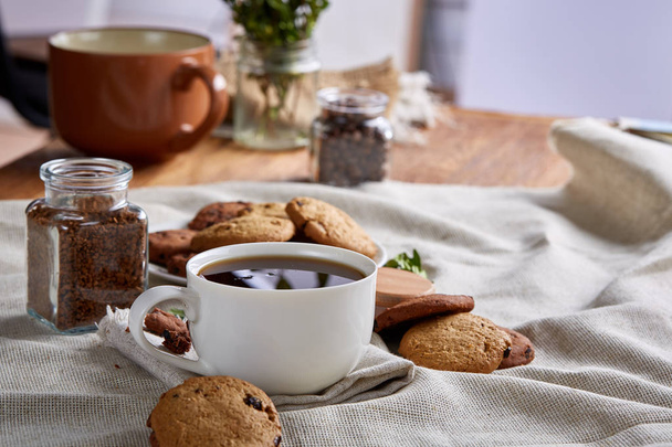 Morning coffee in white cup, chocolate chips cookies on cutting board close-up, selective focus - Фото, зображення