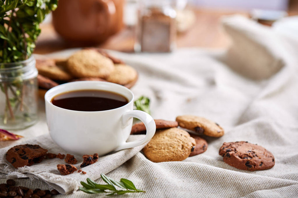 Morning coffee in white cup, chocolate chips cookies on cutting board close-up, selective focus - Fotó, kép