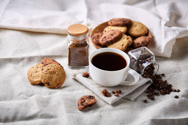 Morning coffee in white cup, chocolate chips cookies on cutting board close-up, selective focus - 写真・画像