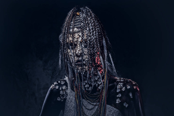Porträt einer furchterregenden afrikanischen Schamanin mit versteinerter rissiger Haut und Dreadlocks auf dunklem Hintergrund. Make-up-Konzept. - Foto, Bild